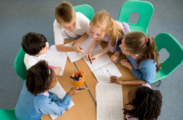 6 students sitting around a table writing in composition notebooks